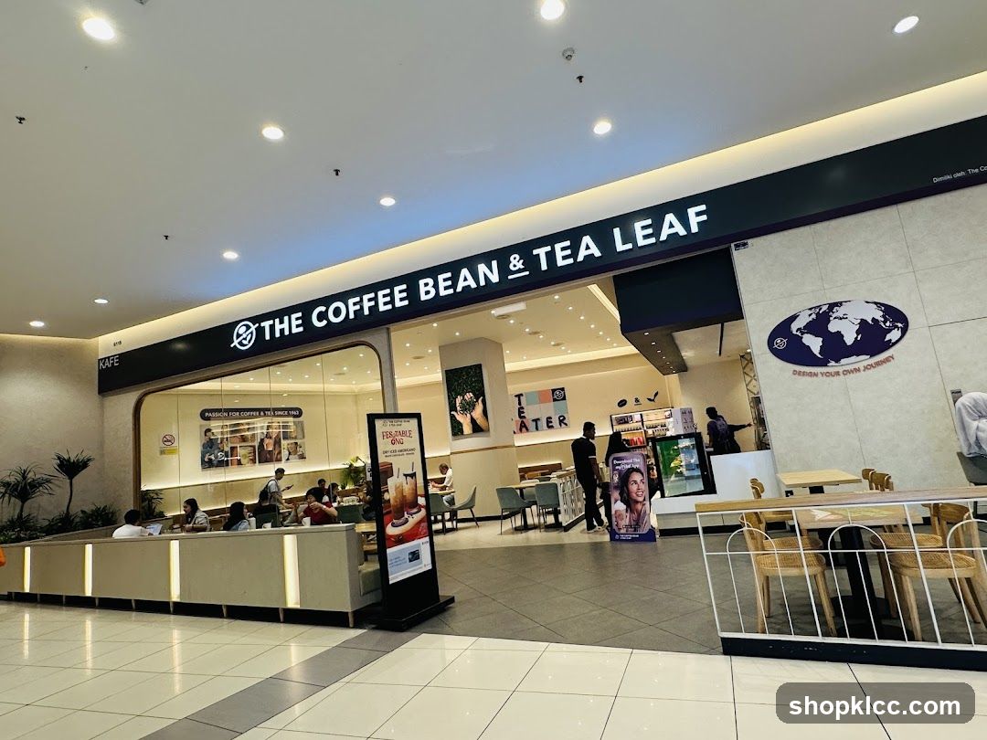 The exterior of a Coffee Bean & Tea Leaf cafe. The prominent signage above the entrance reads "THE COFFEE BEAN & TEA LEAF". Inside, customers are seated at tables. A promotional stand with an image of a drink is placed outside the entrance.