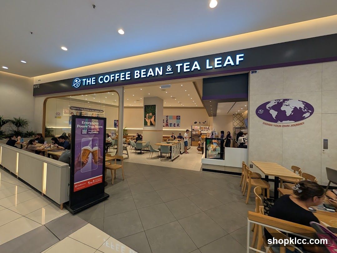 The exterior of a Coffee Bean & Tea Leaf cafe. The prominent sign above the entrance reads "THE COFFEE BEAN & TEA LEAF". Inside, customers are seated at tables, and staff are visible behind the counter. A digital display board outside advertises a promotion.