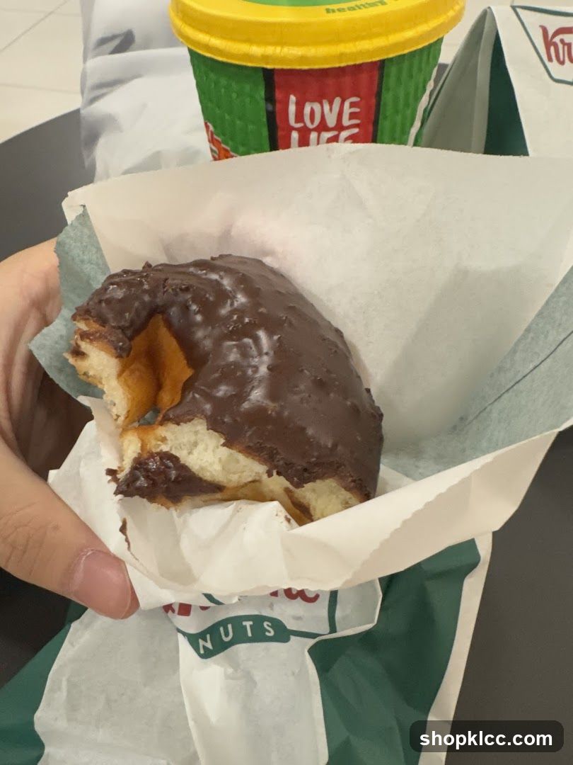 Hand holding chocolate-frosted donut with coffee cup in background