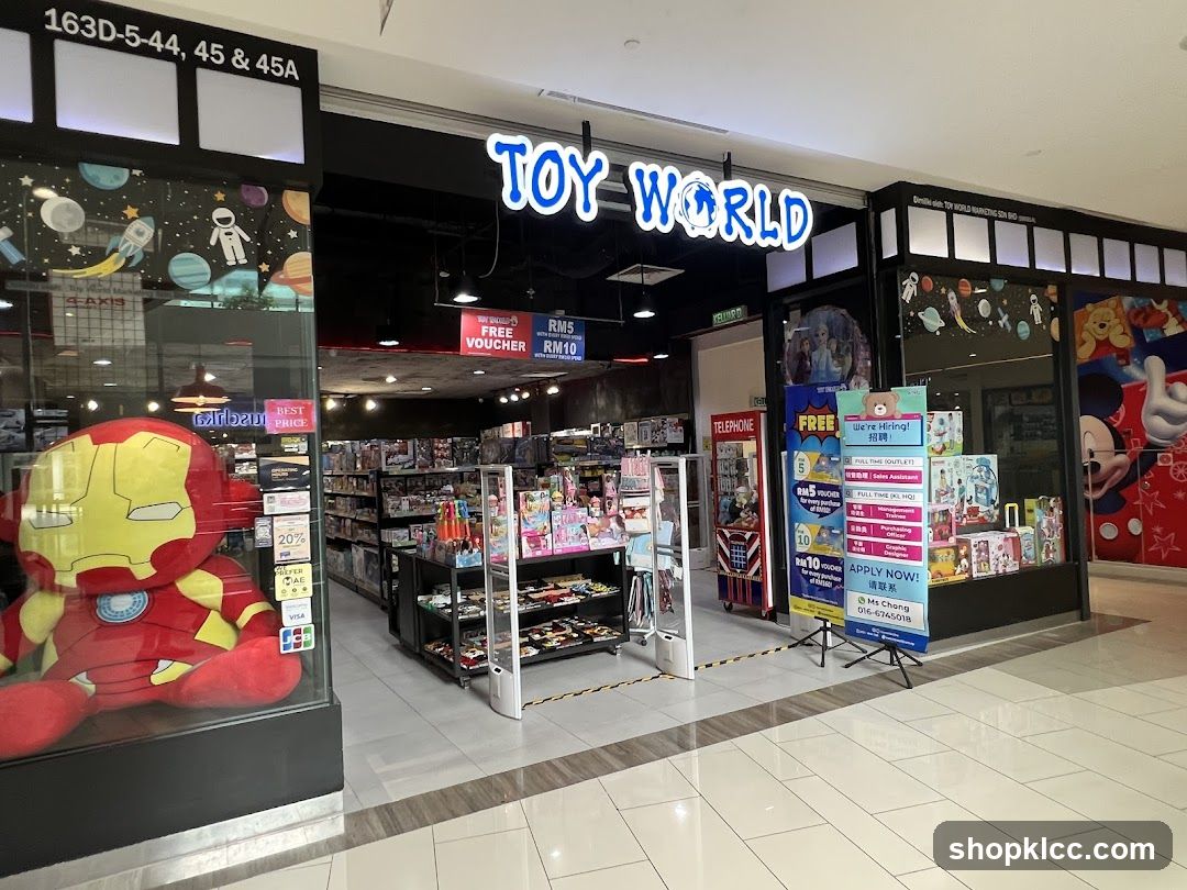 Store entrance with illuminated "TOY WORLD" sign above the doorway. Large Iron Man plush toy displayed on left window. Interior shelves stocked with toys visible. Promotional signs and hiring posters placed outside entrance.