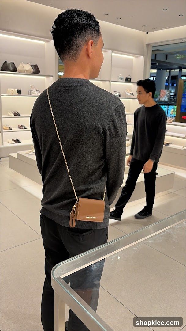 Man wearing a grey sweater and black pants with a brown purse