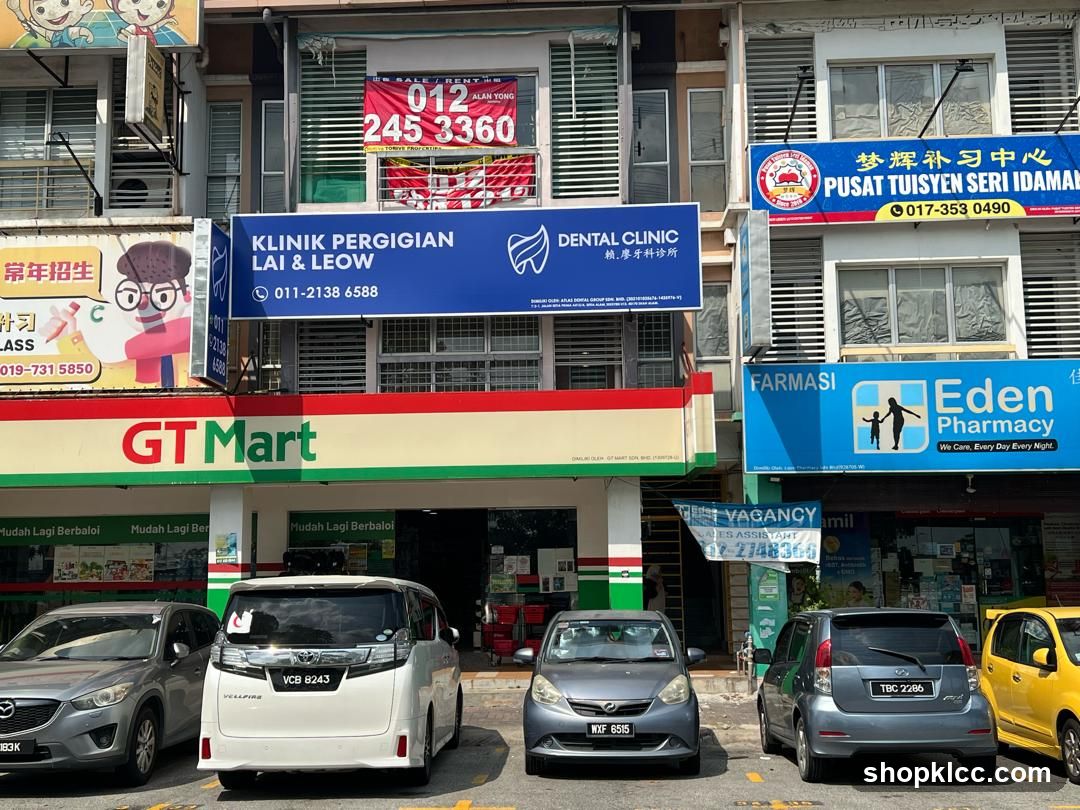 A row of shops with various businesses. The GT Mart grocery store is prominently displayed with its red and green signage. To its left, a dental clinic named Lai & Leow is visible with blue signage. Further to the right, an Eden Pharmacy is advertised with blue and white branding. Other businesses include a tuition center and a "For Sale/Rent" sign. Cars are parked in front of the shops.