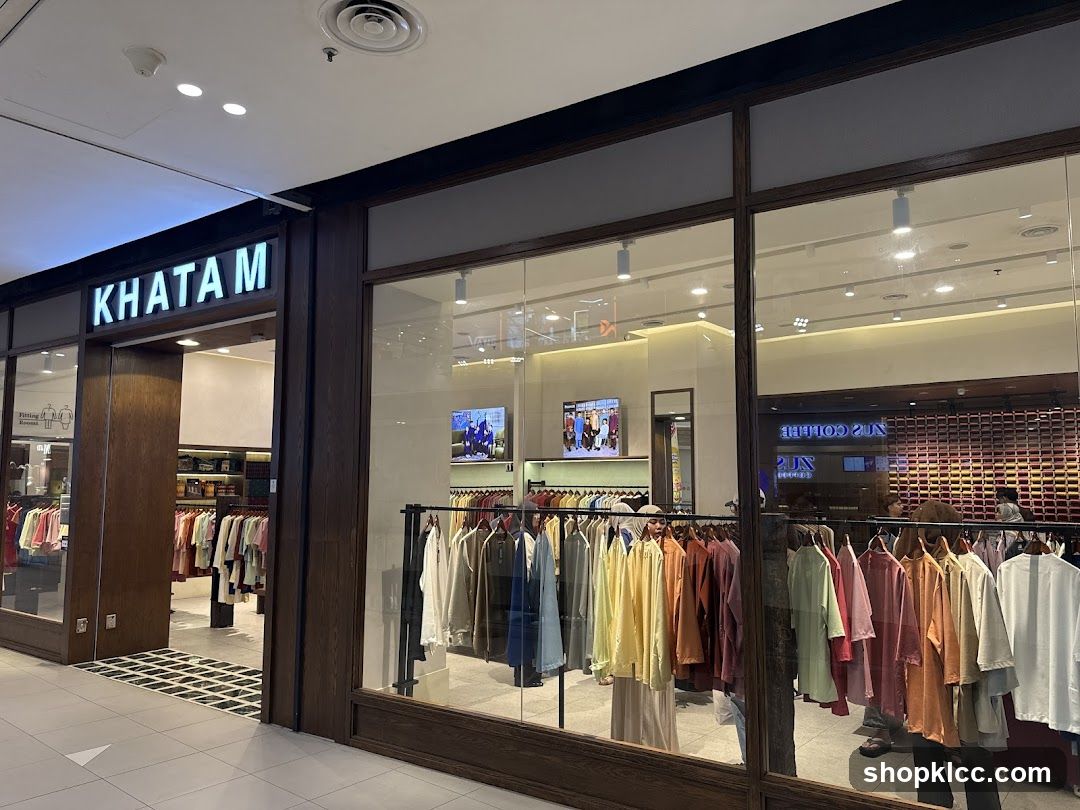 The exterior of a clothing store with the name KHATAM displayed prominently above the entrance. Racks of colorful garments are visible both inside the store and displayed in the large front windows.