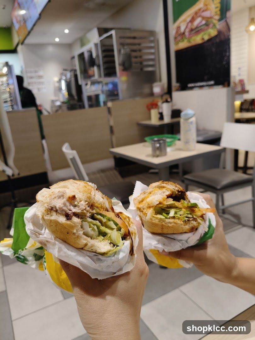 Two sandwiches held up in front of a Subway restaurant