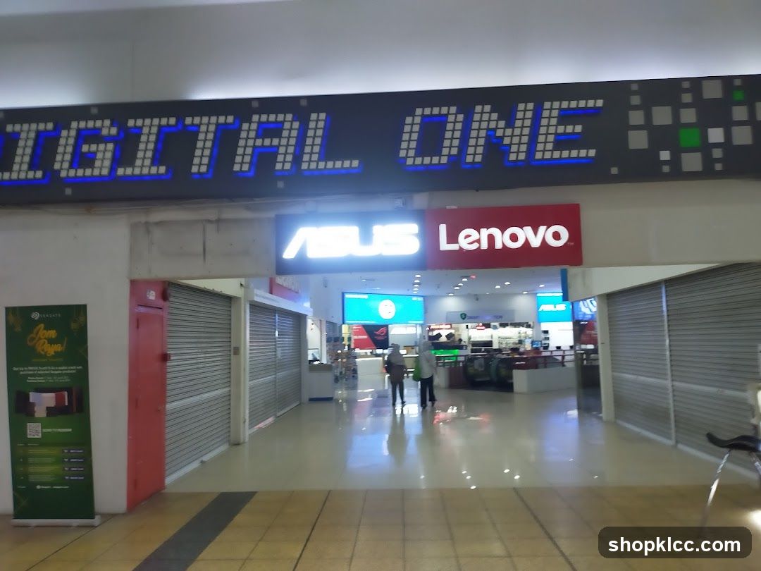 The exterior of a store with a large digital sign above that reads "DIGITAL ONE". Below this, there are signs for "ASUS" and "Lenovo". The store appears to be an electronics retailer, with displays visible inside. There are closed shutters on either side of the entrance. A promotional banner for Seagate is visible to the left.