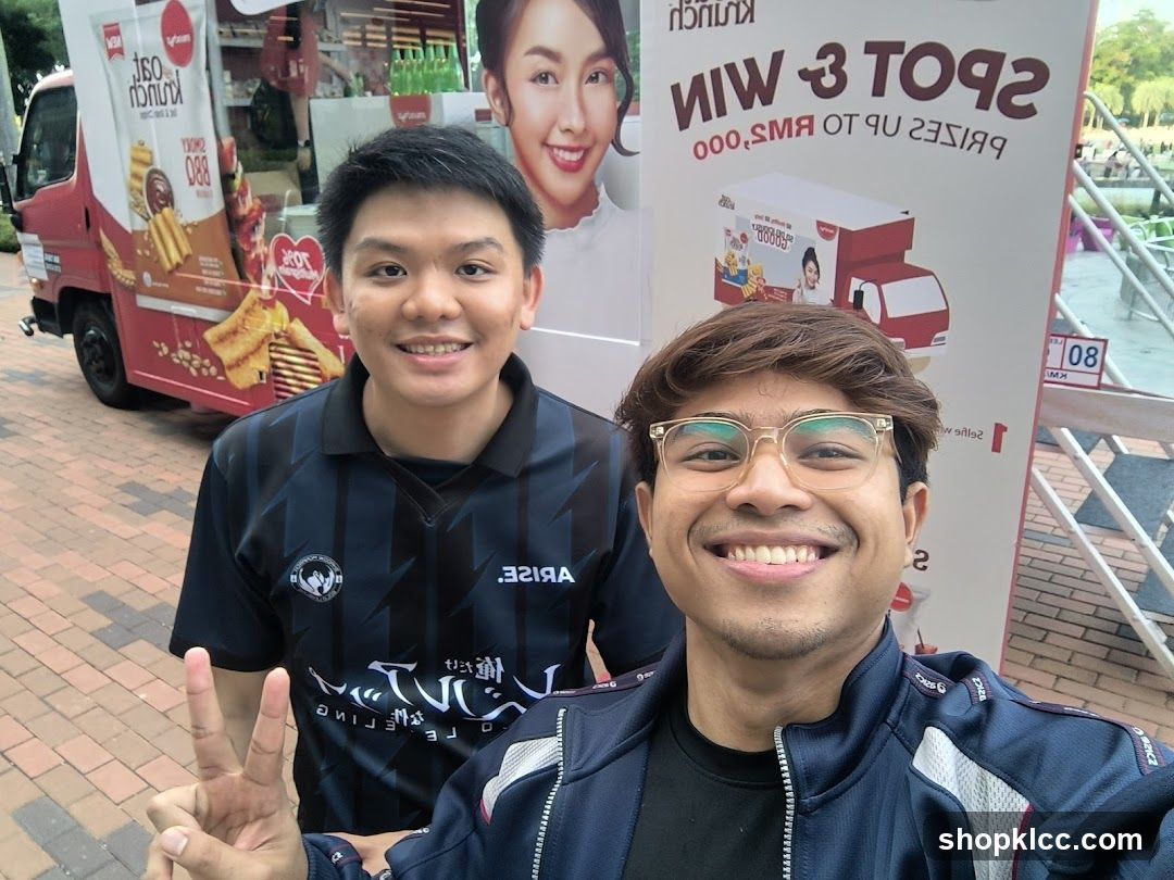Two men posing for a selfie in front of a promotional truck and banner