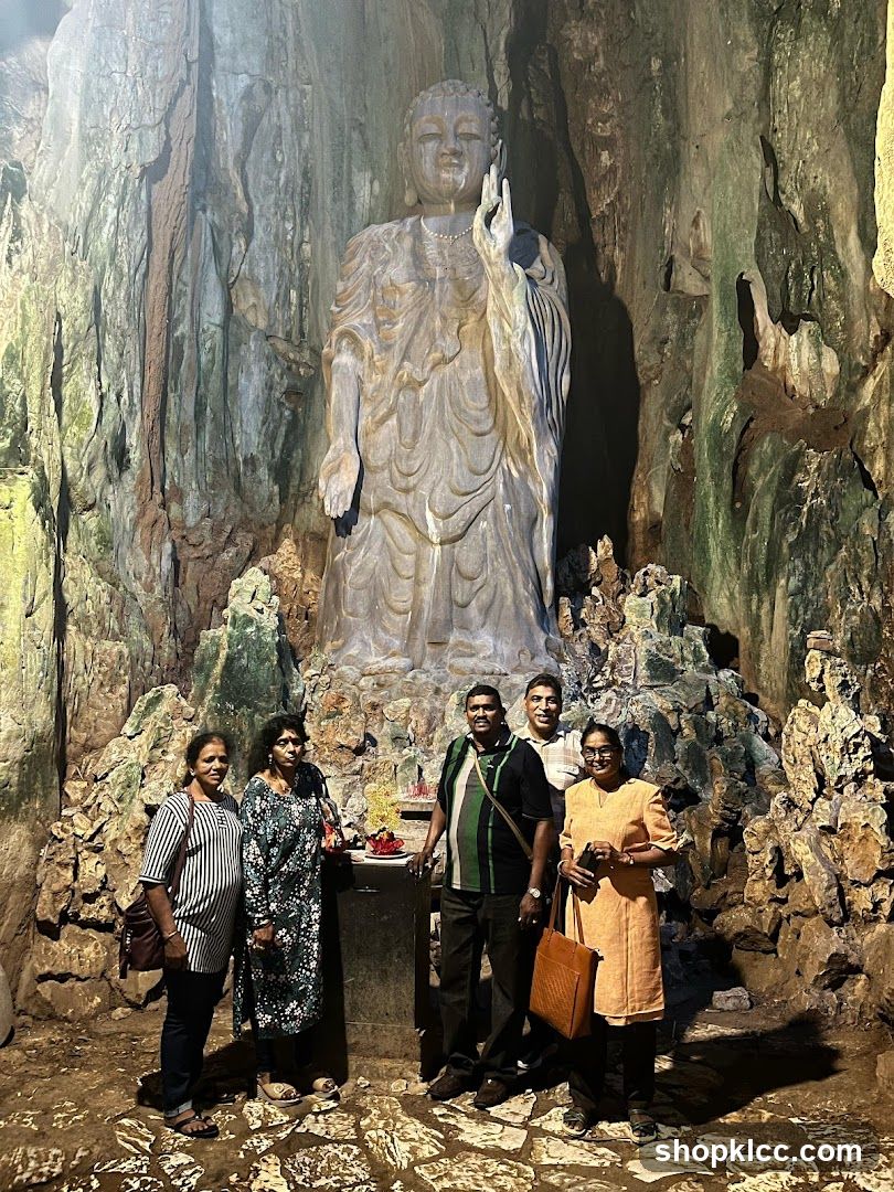 People Posing in Front of a Large Buddha Statue in a Cave