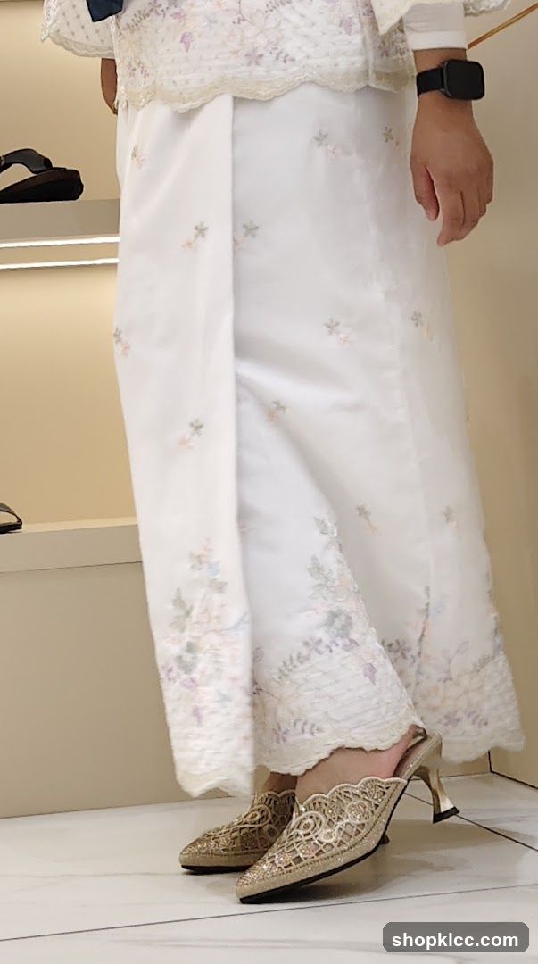 Woman wearing embroidered white outfit and gold heels
