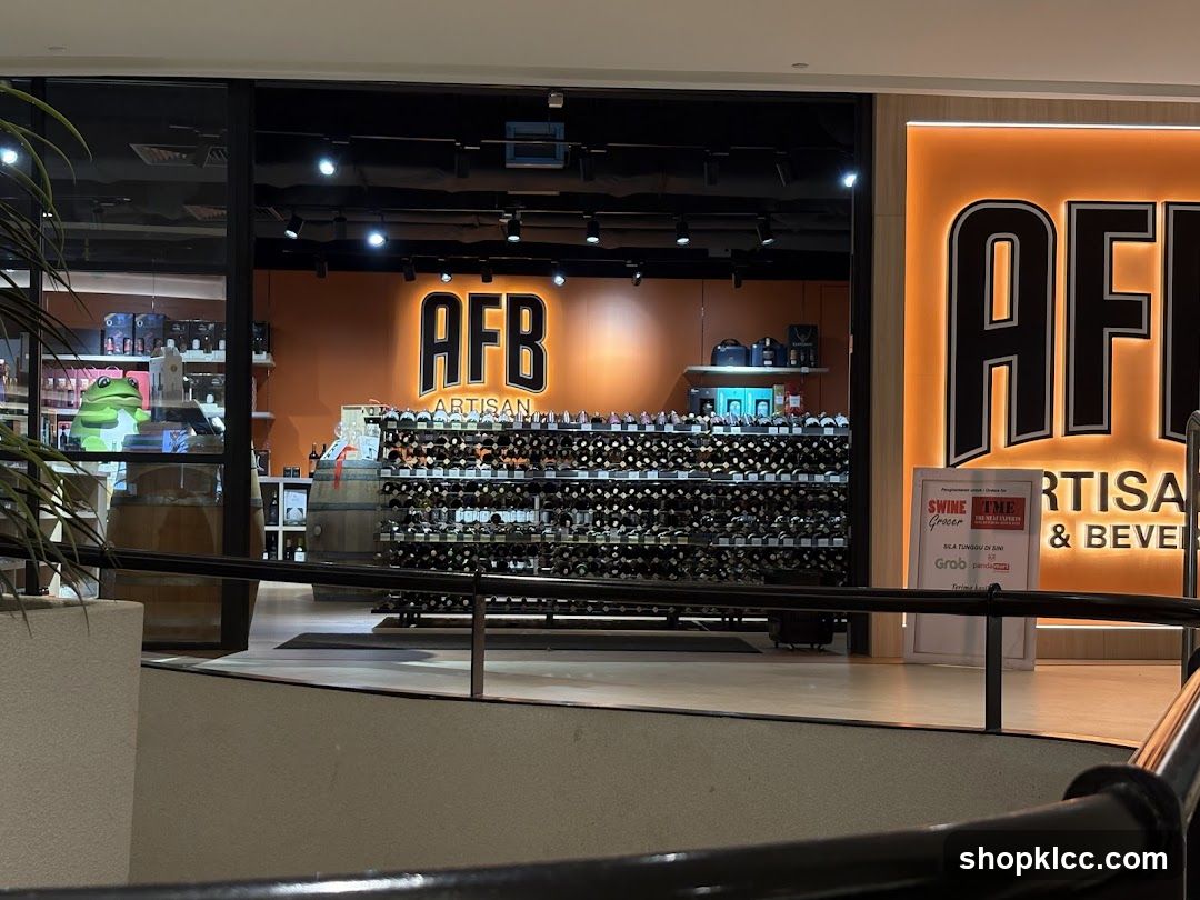 The storefront of AFB Artisan & Beverages, a store selling wine and other beverages. The store has a large orange sign with the letters "AFB" in black. Inside, shelves are stocked with numerous bottles of wine. A large green frog decoration is visible in the window. A sign near the entrance advertises "SWINE TME Grocer" and mentions delivery services like Grab and Panda.