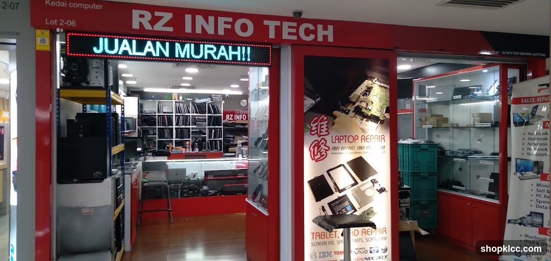 The storefront of RZ INFO TECH, a computer store. An LED sign above the entrance displays "JUALAN MURAH!!". The shop displays computers, laptops, and computer parts. A poster advertises laptop and tablet repair services.