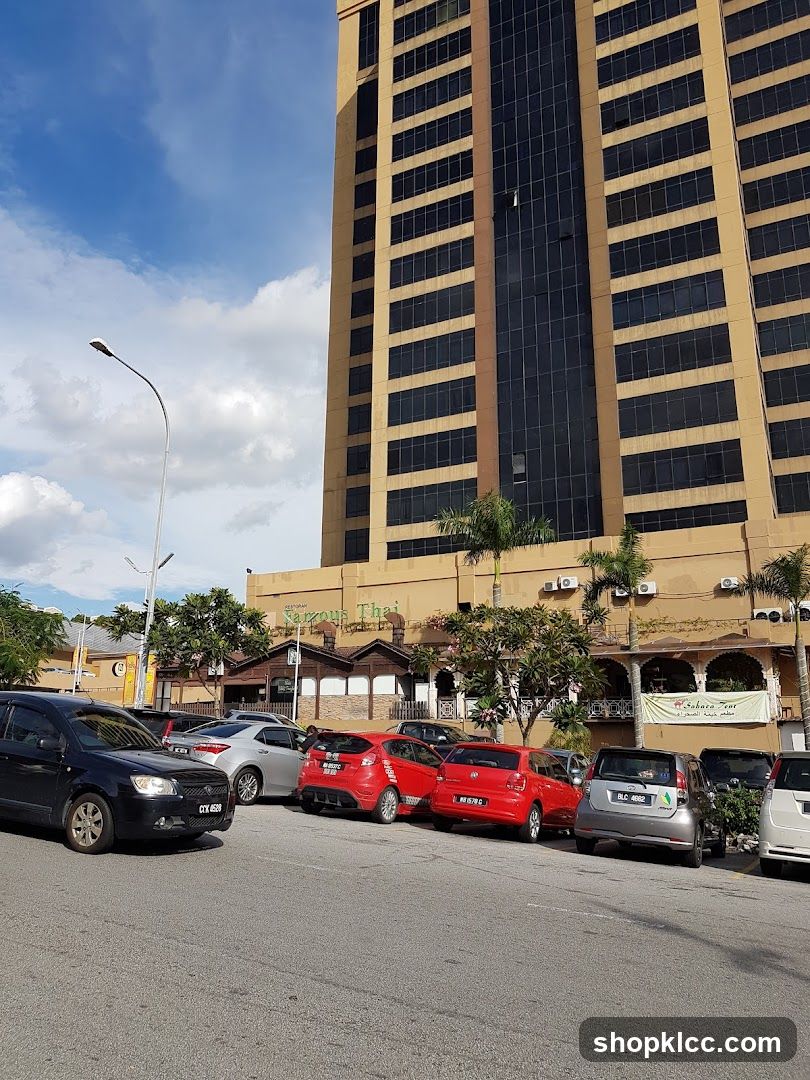 A low-rise building with a tan facade is visible in front of a tall, modern building. The lower building has a sign that reads "RESTAURANT Narrous Thai". There are several cars parked in front of the building.