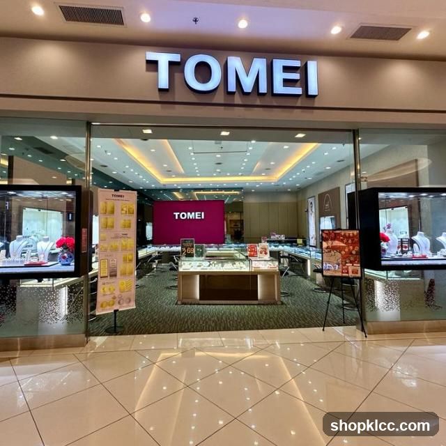The exterior of a Tomei jewelry store, with the brand name prominently displayed in large illuminated letters above the entrance. The store features large display windows showcasing jewelry on mannequins and in cases. Inside, more display cases and a large screen displaying the Tomei logo are visible.
