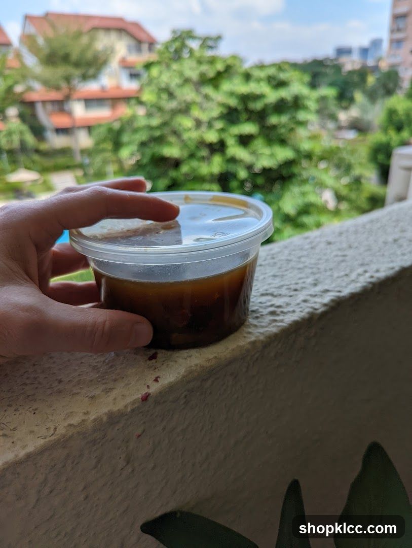 Hand holding a container of dark liquid on a balcony ledge