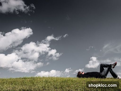 Person Lying on Grass Under Cloudy Sky