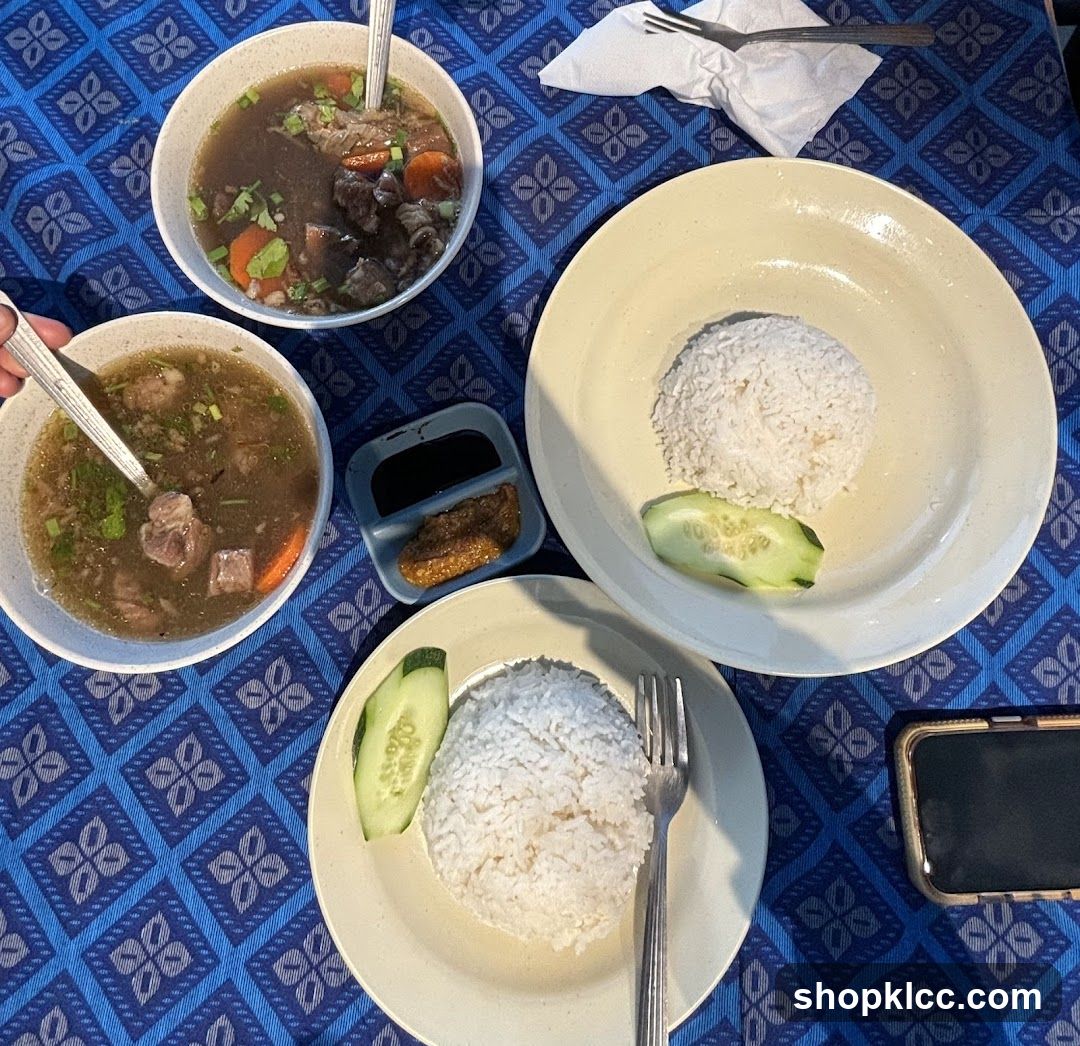 Two bowls of soup with meat and vegetables, and two plates of rice with cucumber slices and a small dish of sauce.
