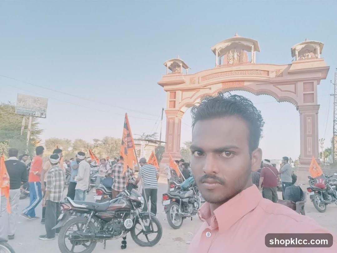 Man taking a selfie in front of a large archway with a crowd and flags