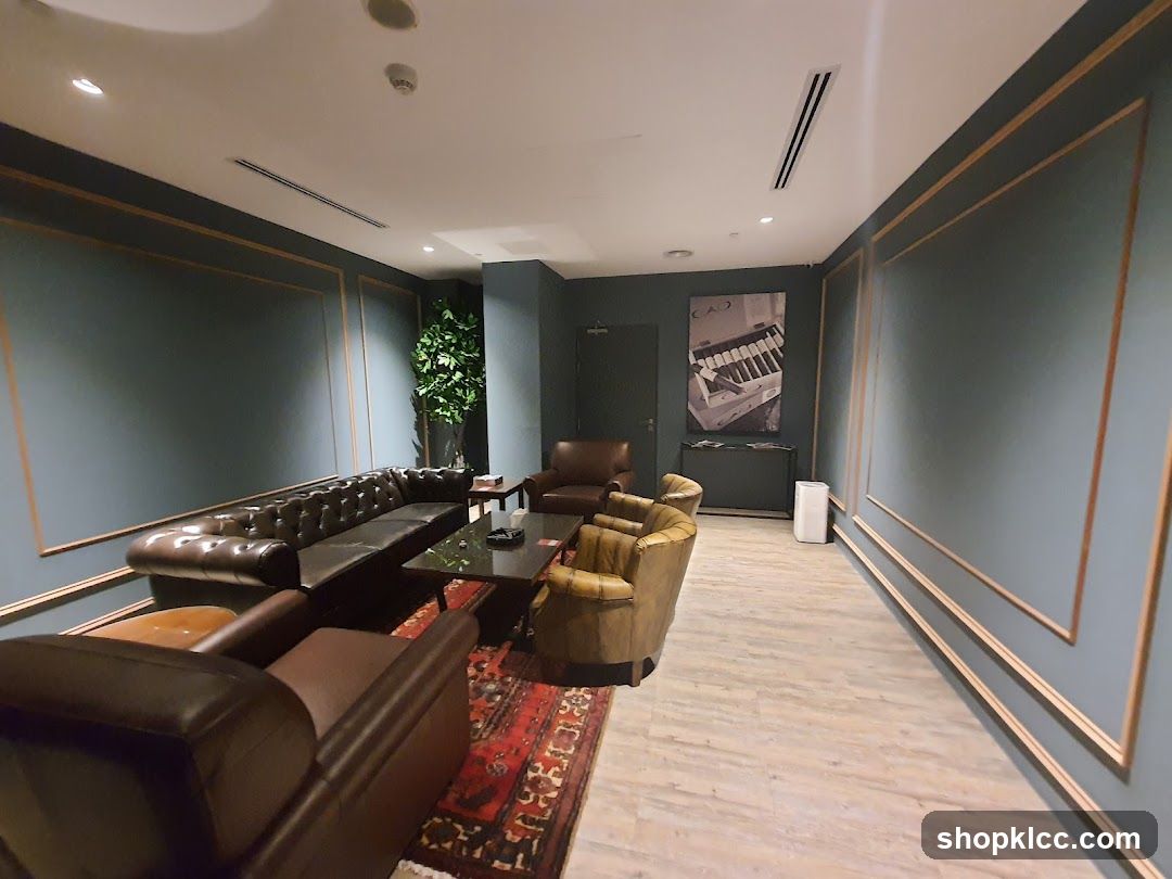 A sophisticated lounge area with dark teal walls, ornate gold trim, and plush leather seating. A large tufted sofa and armchairs are arranged around a dark coffee table, with a Persian rug on the light wood-look floor. A large framed artwork of a piano keyboard hangs on the wall, and a tall potted plant adds a touch of greenery. The room is well-lit with recessed ceiling lights.