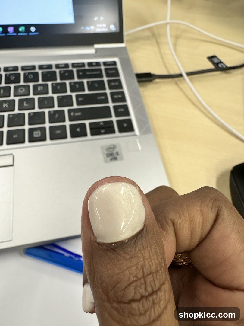 Close-up of a person's thumb with a light-colored nail polish, next to a laptop keyboard.