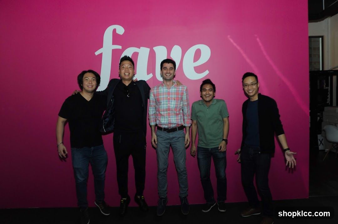 Five men posing in front of a pink wall with a logo