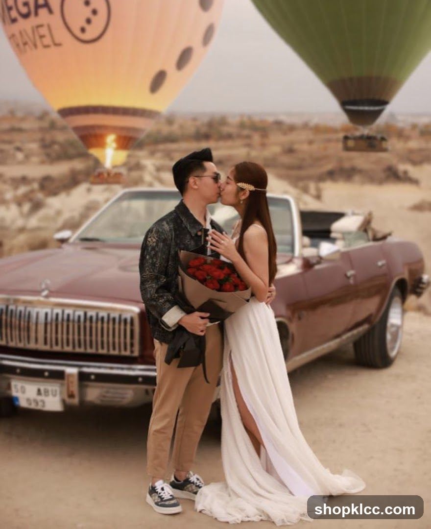 Couple kissing in front of hot air balloons and a vintage car