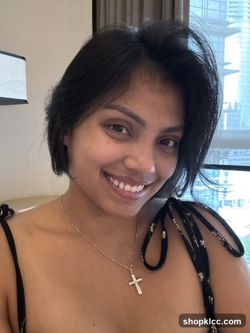 Portrait of a woman with short dark hair smiling at the camera, wearing a necklace with a cross pendant and a black top with floral straps.
