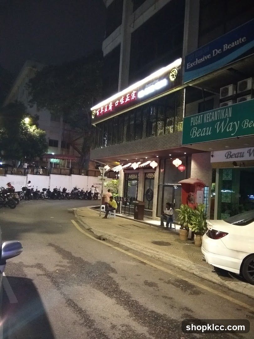 Nighttime street view of storefronts with illuminated signage and parked vehicles.