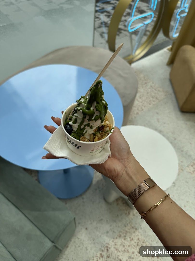 Hand holding a dessert cup with green drizzle and toppings