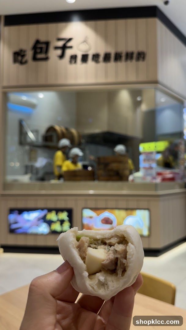 Hand holding a steamed bun in front of a bakery counter