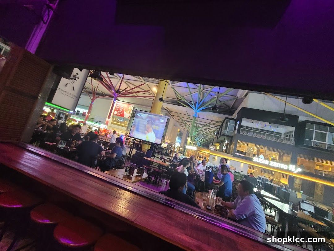 People dining at tables in a lively outdoor area with screens showing sports