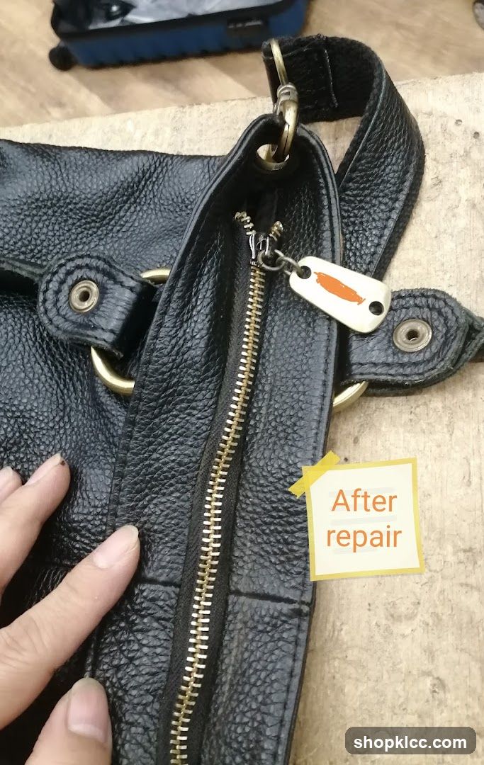 Hand holding a black leather bag with a repaired zipper