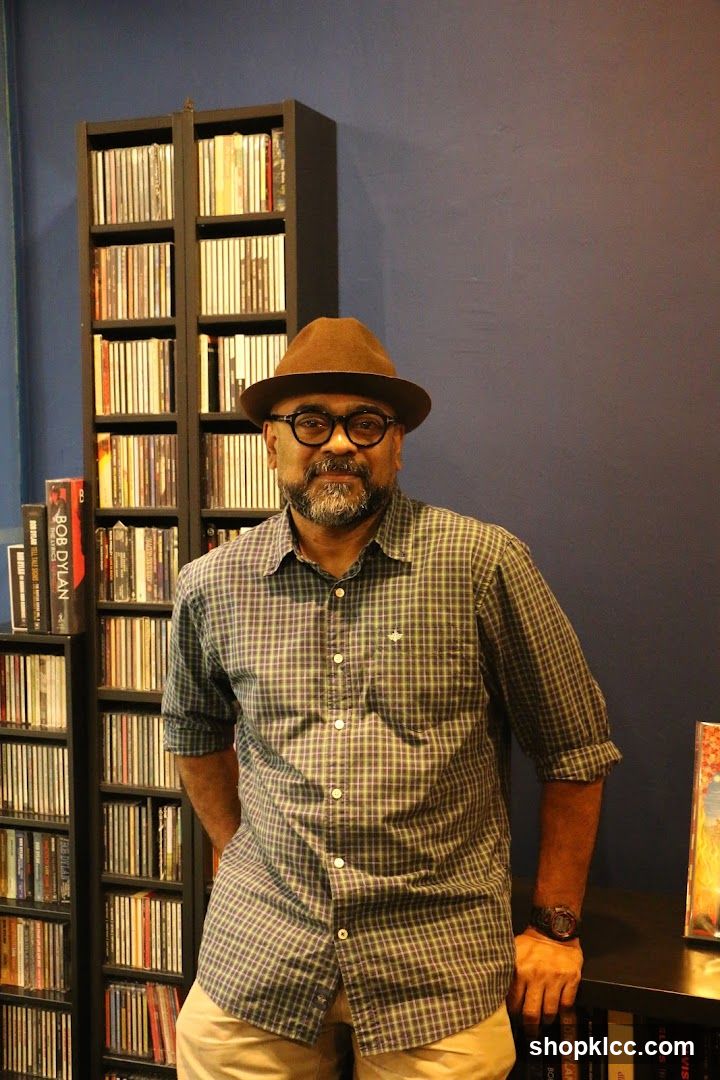 Man in Hat and Plaid Shirt Posed in Front of CD Shelves