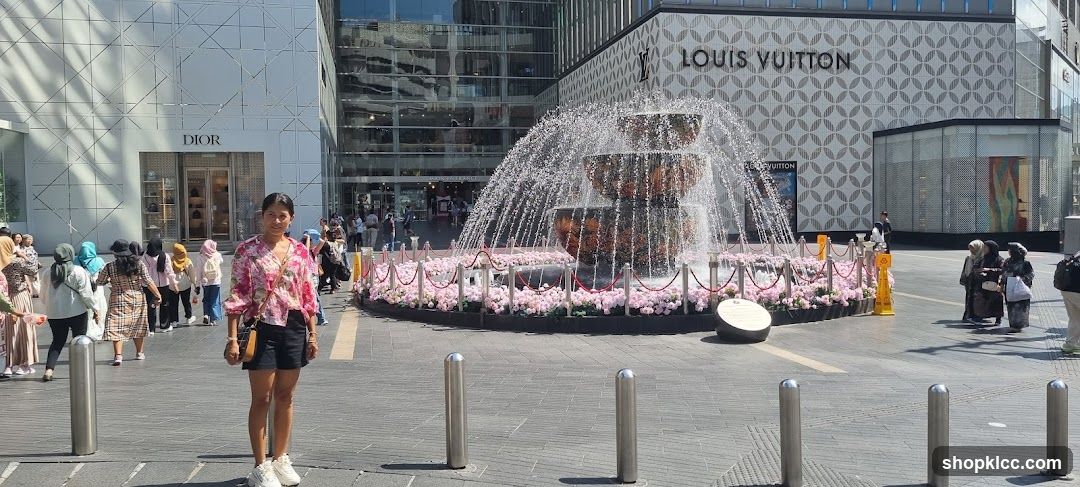 Woman Poses in Front of Fountain and Luxury Stores