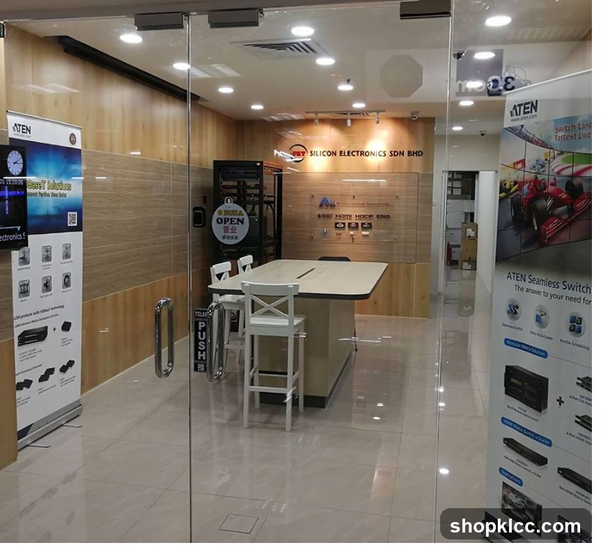 A view through a glass door into a modern office space. The office features a large conference table with chairs, wooden paneling on the walls, and various electronic equipment and displays. Promotional banners for ATEN products are visible on the left and right sides of the entrance.