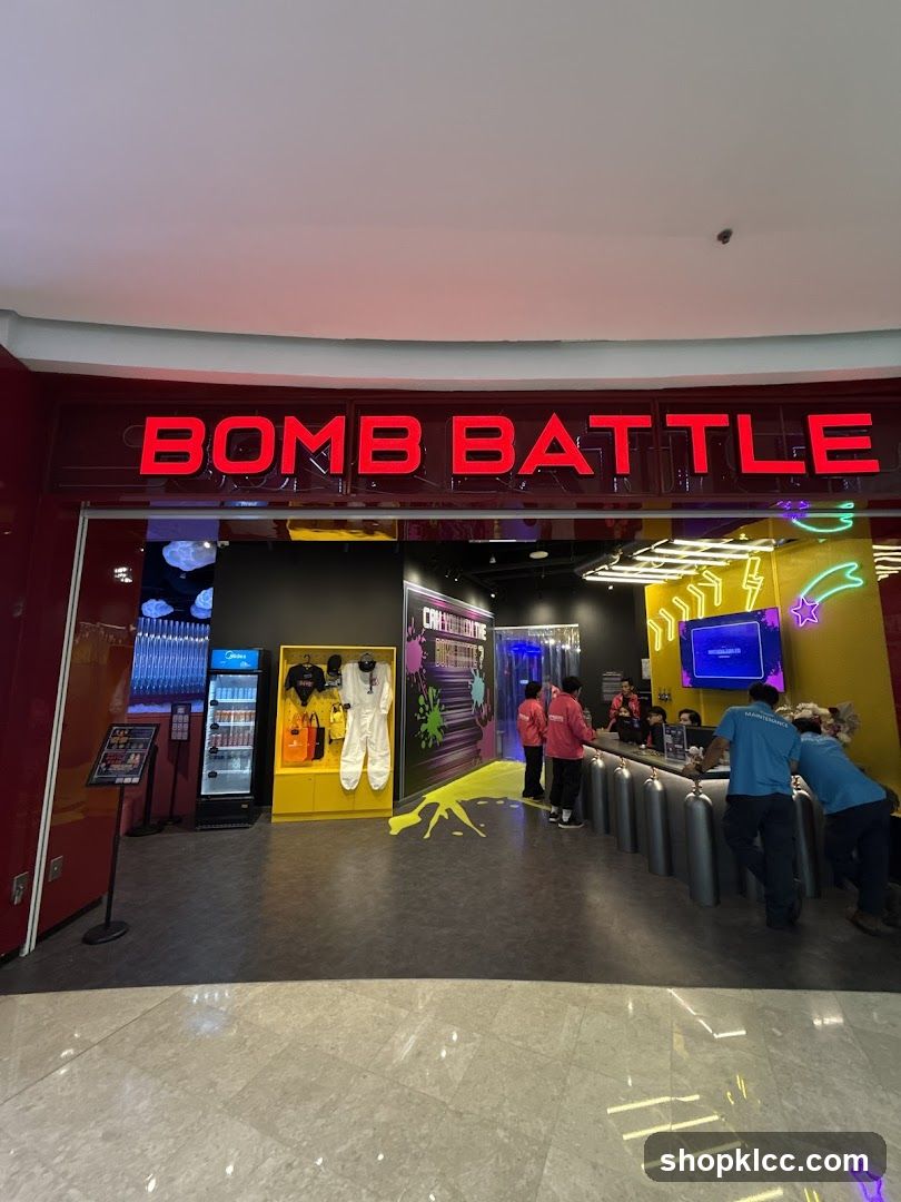 The exterior of a Bomb Battle store. Red neon letters spell out "BOMB BATTLE" above the entrance. Inside, there is a display of merchandise including jumpsuits and bags, a refrigerator stocked with drinks, and a counter with staff members. The floor is dark grey with yellow splattered paint designs.