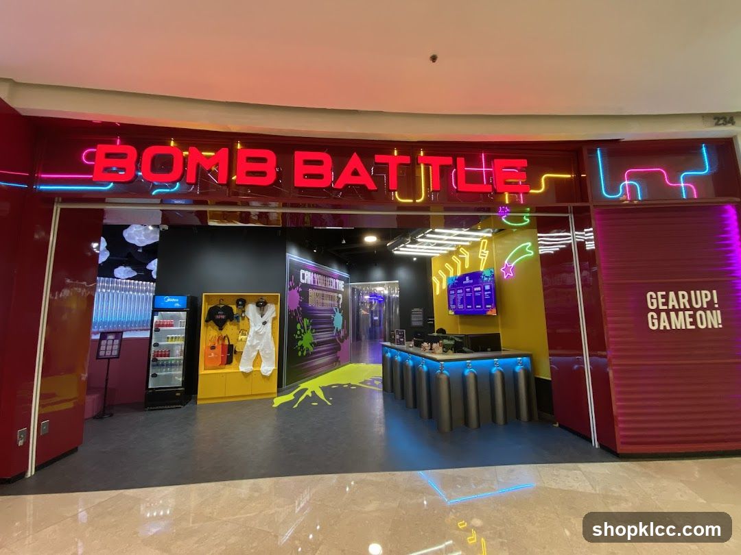 The exterior of a Bomb Battle store with neon signage. The entrance is open, revealing a counter area with staff, a display of merchandise including a white jumpsuit and t-shirts, and a cooler stocked with drinks. A screen displays what appears to be a menu or game information. The overall aesthetic is vibrant and modern, with colorful lighting and graphics.