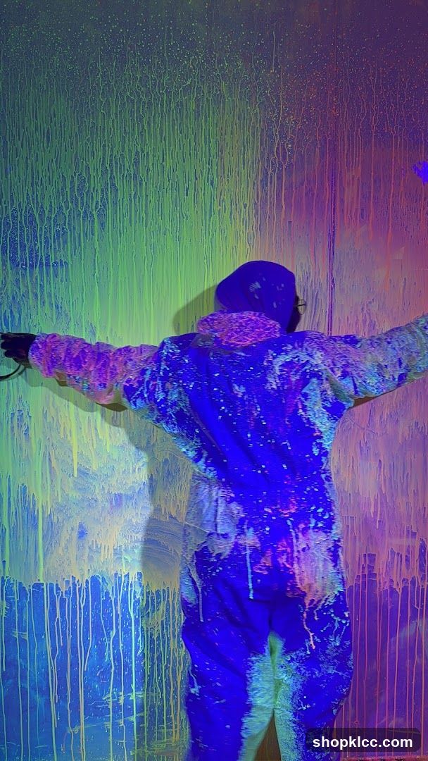 Person in paint-splattered suit in a neon-lit room