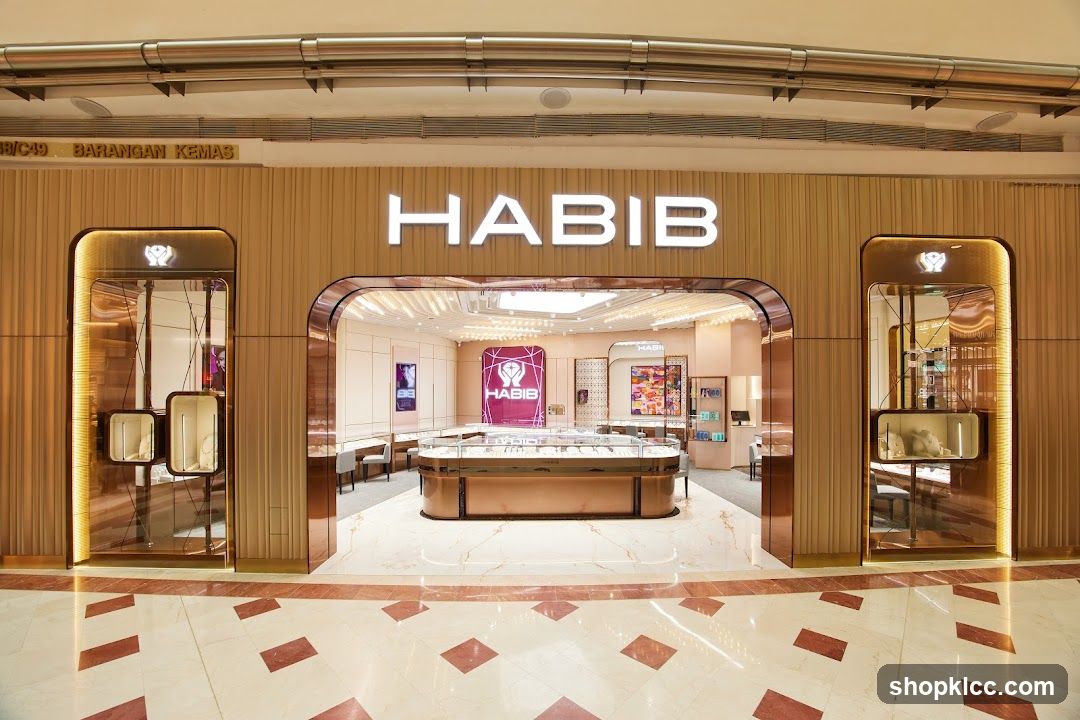 The exterior of a Habib jewelry store, featuring a large illuminated sign with the store name. The entrance is wide and inviting, with display cases visible inside showcasing jewelry. The store's facade is modern and elegant, with warm wood tones and metallic accents.