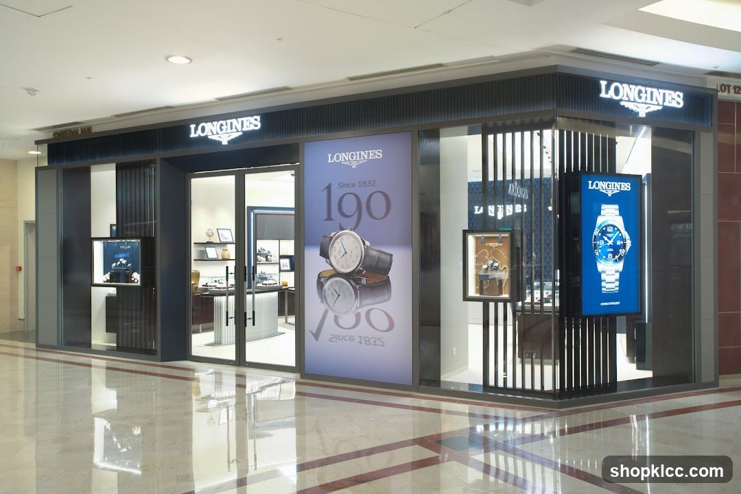 The exterior of a Longines watch store. The store has large glass windows and doors, with prominent Longines signage above the entrance. Inside, display cases showcase watches. A large advertisement featuring a Longines watch is displayed on the front of the store.