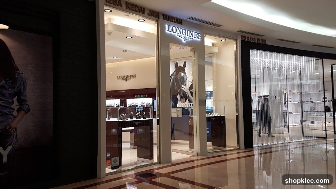 The exterior of a Longines watch store. The store has a modern design with large glass windows displaying watches. A large advertisement featuring a horse and rider is visible inside the store. The Longines logo is prominently displayed above the entrance.
