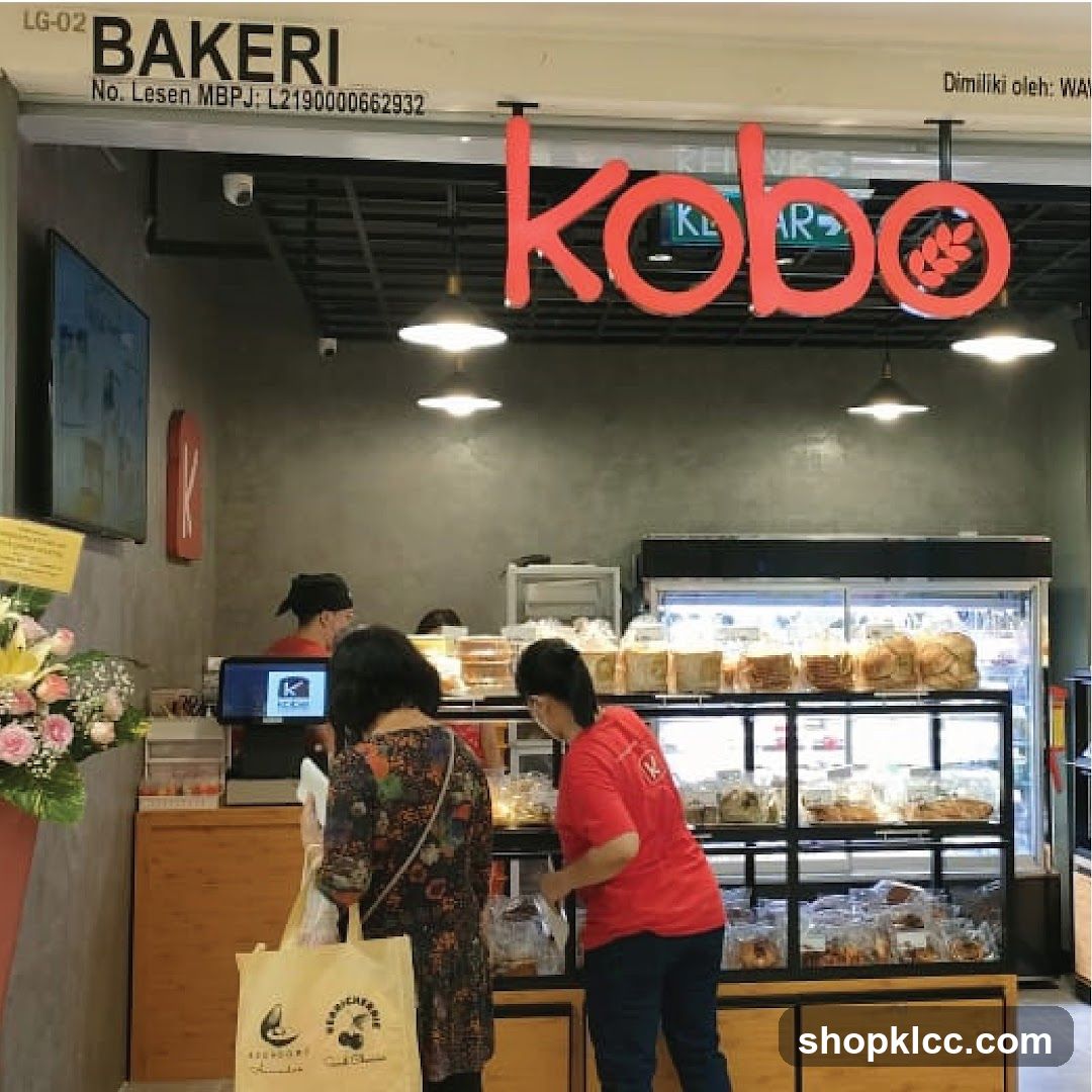 The exterior of a bakery with a large red "kobo" sign above the entrance. Inside, shelves are stocked with various baked goods. Customers are seen browsing and purchasing items.