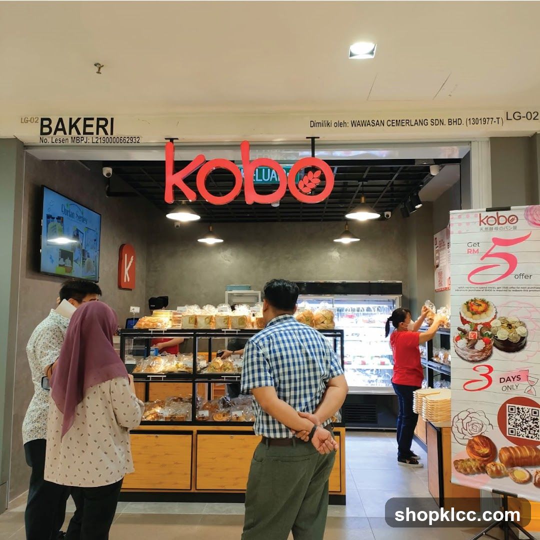 The exterior of a bakery with a large red "kobo" sign above the entrance. Inside, shelves are stocked with various baked goods, and customers are browsing. A promotional poster for a "Get RM5 offer" is displayed on the right.