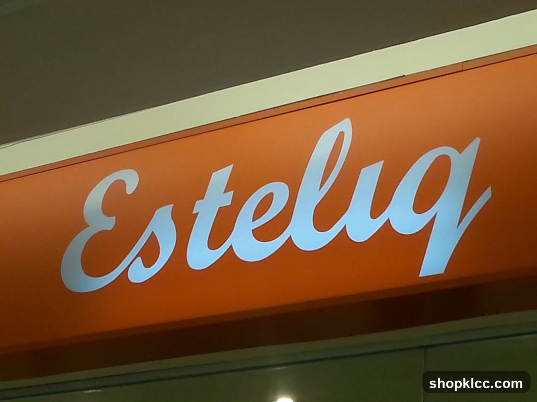 A close-up shot of an illuminated orange sign with the word "Estelug" written in white cursive script. The sign appears to be mounted above a storefront.