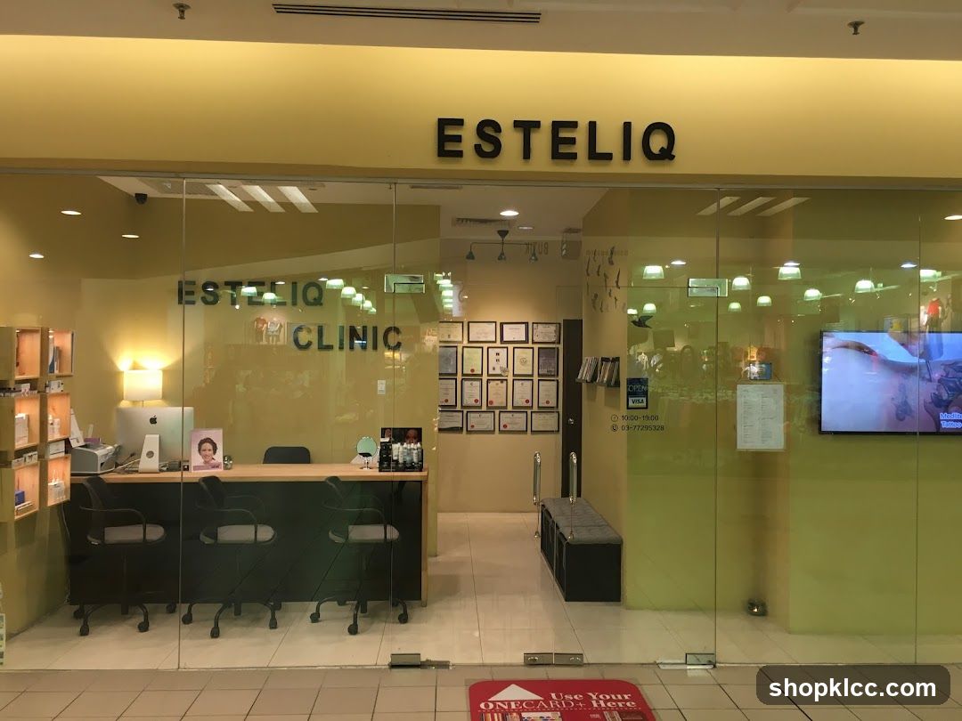 The exterior of a clinic with a large glass storefront. The name ESTELIQ is displayed in large black letters above the entrance. Inside, a reception desk with chairs is visible, along with framed certificates on the wall. A television screen is mounted on the right side of the storefront.