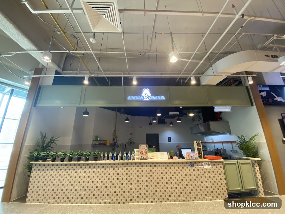 A view of the Anna Omar storefront, featuring a counter with potted plants and bottles, and the Anna Omar logo illuminated above.