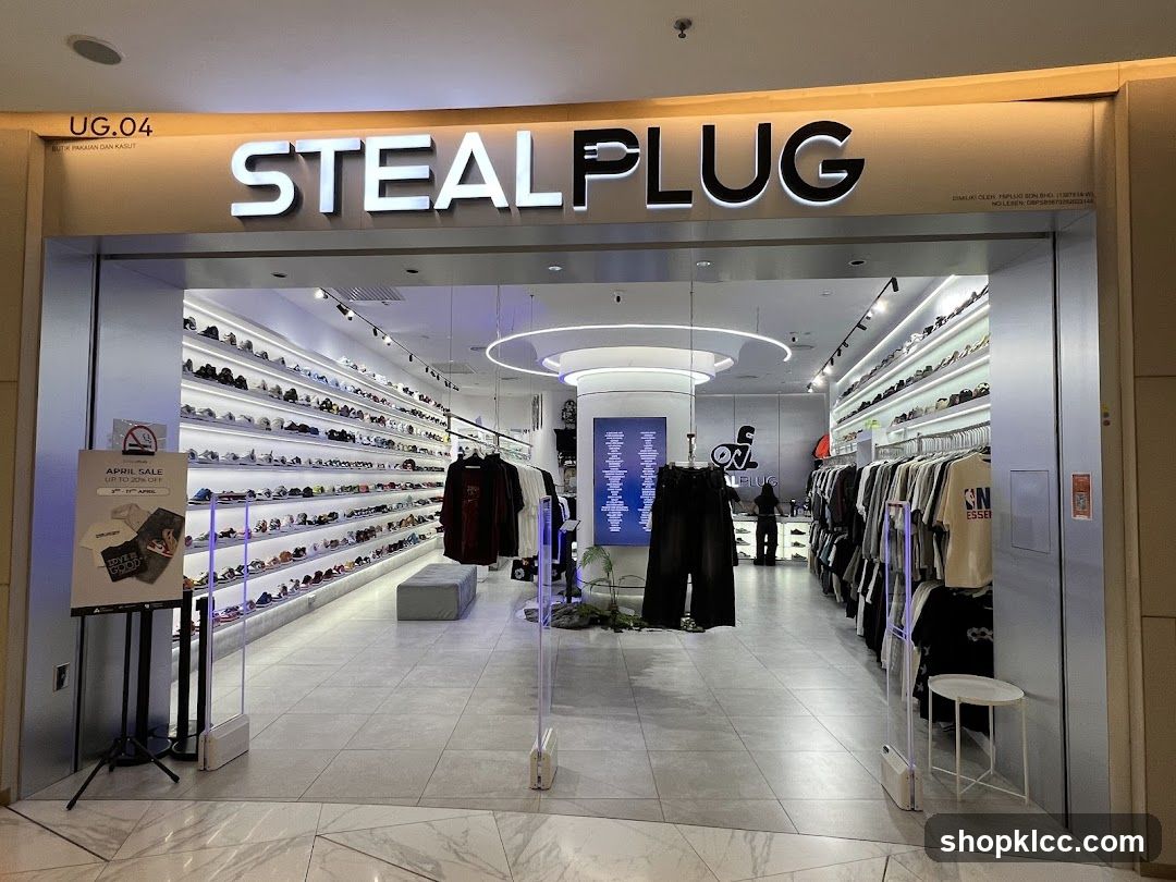 The exterior of a retail store called STEALPLUG, which sells clothing and shoes. The store has a modern facade with large glass windows and a prominent illuminated sign. Inside, shelves are stocked with numerous pairs of shoes, and racks display various apparel items.