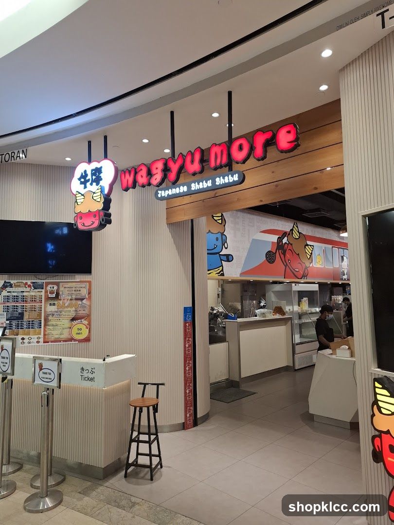 The exterior of a Wagyu More Japanese Shabu Shabu restaurant. The sign above the entrance reads "wagyu more" in red neon letters, with "Japanese Shabu Shabu" below it. A cartoon character with horns and a red face is part of the signage. To the left, a menu board displays prices and meal deals. Inside, staff can be seen working behind a counter.