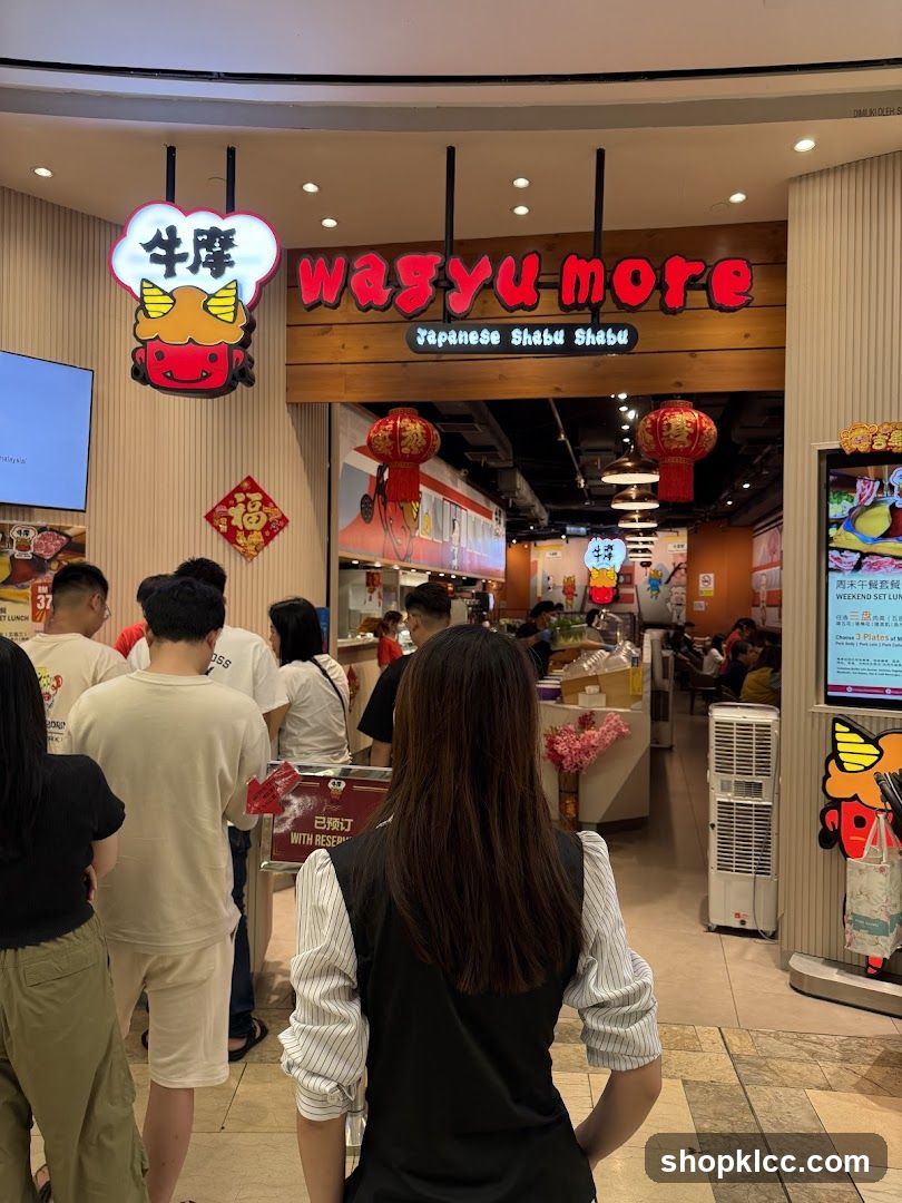 The exterior of a Japanese Shabu Shabu restaurant called Wagyu More. A red sign with the name "wagyumore" is visible above the entrance, along with a cartoon bull character. People are queuing to enter the restaurant.