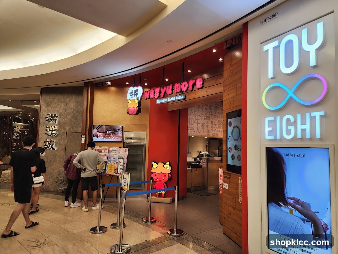 The exterior of a Japanese shabu shabu restaurant called Wagyu More. The entrance is red with wooden accents. A sign with the restaurant's name and logo is visible above the entrance. To the right, a sign for "TOY EIGHT" with an infinity symbol is displayed. Several people are walking by or looking at menus outside the restaurant.