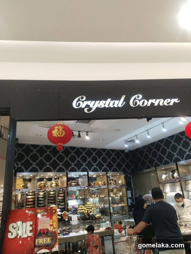 Storefront with black sign bearing white cursive 'Crystal Corner' logo. Interior features dark patterned wallpaper, glass display cases filled with crystals and decorative items, red lanterns hanging from ceiling. Customers are inside browsing merchandise. A red promotional poster with 'SALE' and 'FREE' is visible on the left.