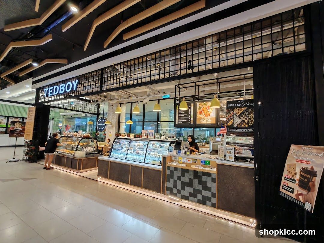 A view of the Tedboy bakery storefront, showcasing a display of pastries and cakes. A staff member is visible behind the counter. The prominent "TEDBOY" signage is displayed above the entrance.
